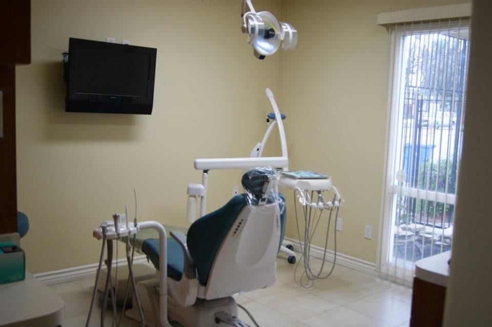 A second treatment room with a teal dental chair, an overhead light and a window looking onto the courtyard greenery